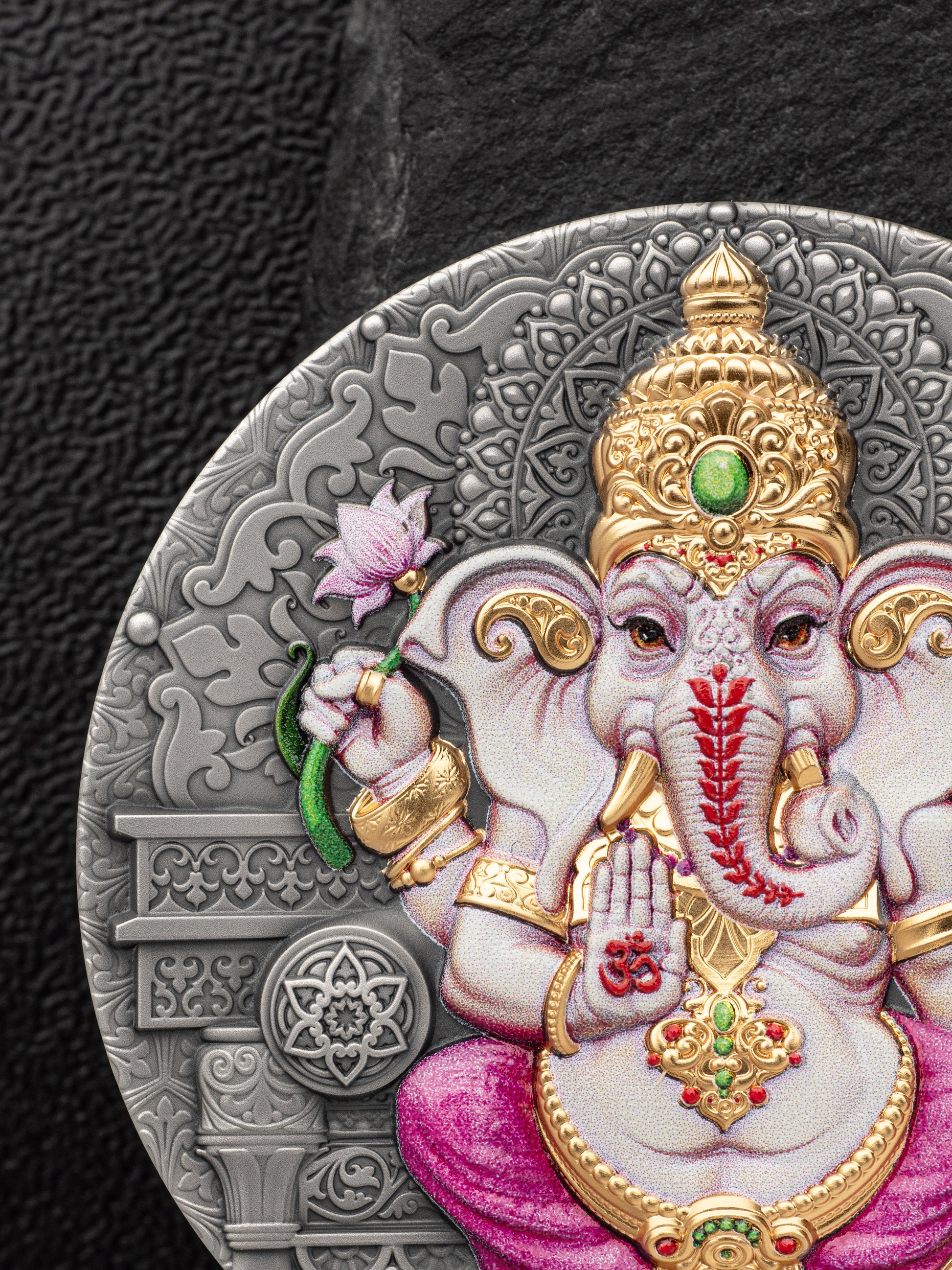 Decorative coin with an intricate design of a deity, featuring gold, pink, and red elements on a dark background.
