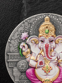 Decorative coin with an intricate design of a deity, featuring gold, pink, and red elements on a dark background.