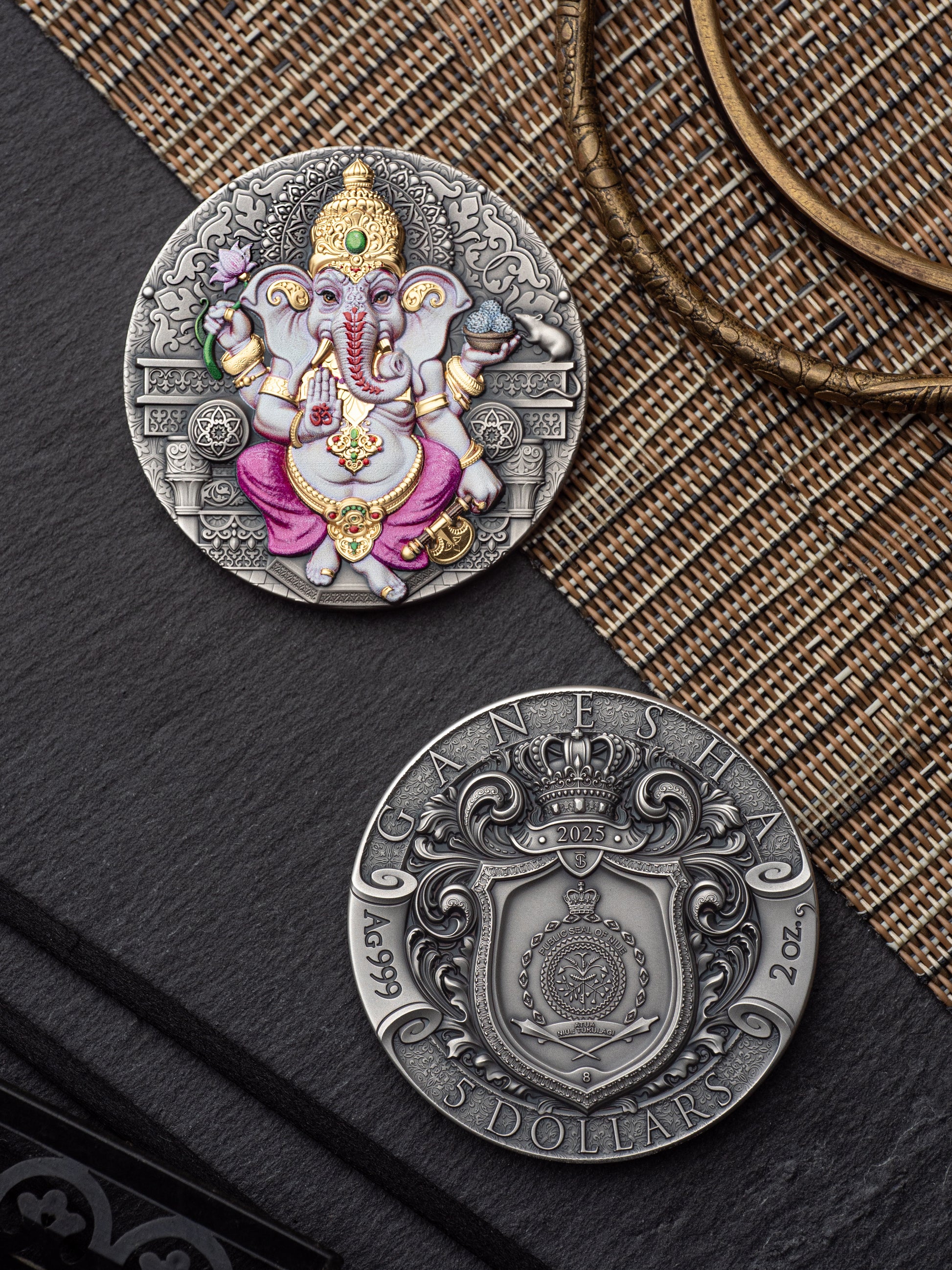 Silver coin with Ganesha figure on one side and embossed design on the other, placed on a textured surface.