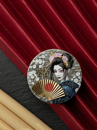 Decorative button with a geisha design on a red and black background