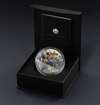 Decorative coin with intricate design in a black box on a dark background
